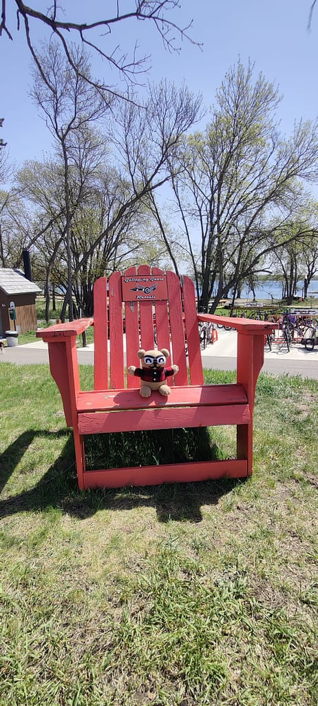 Cardibear sitting on a large red Adirondack chair at the rental center at Glendalough State Park in Battle Lake, MN