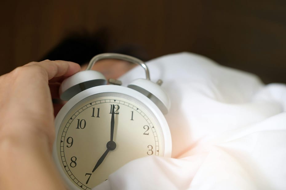 Stock photo of an alarm clock being held by someone who is sleeping